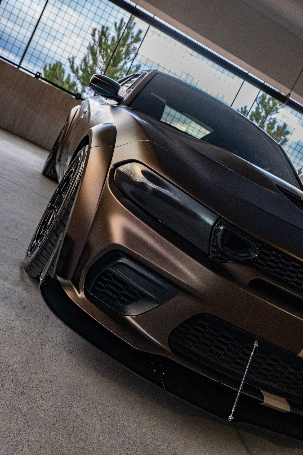 Low-angle close-up of matte brown Charger headlight, splitter, and forged wheel