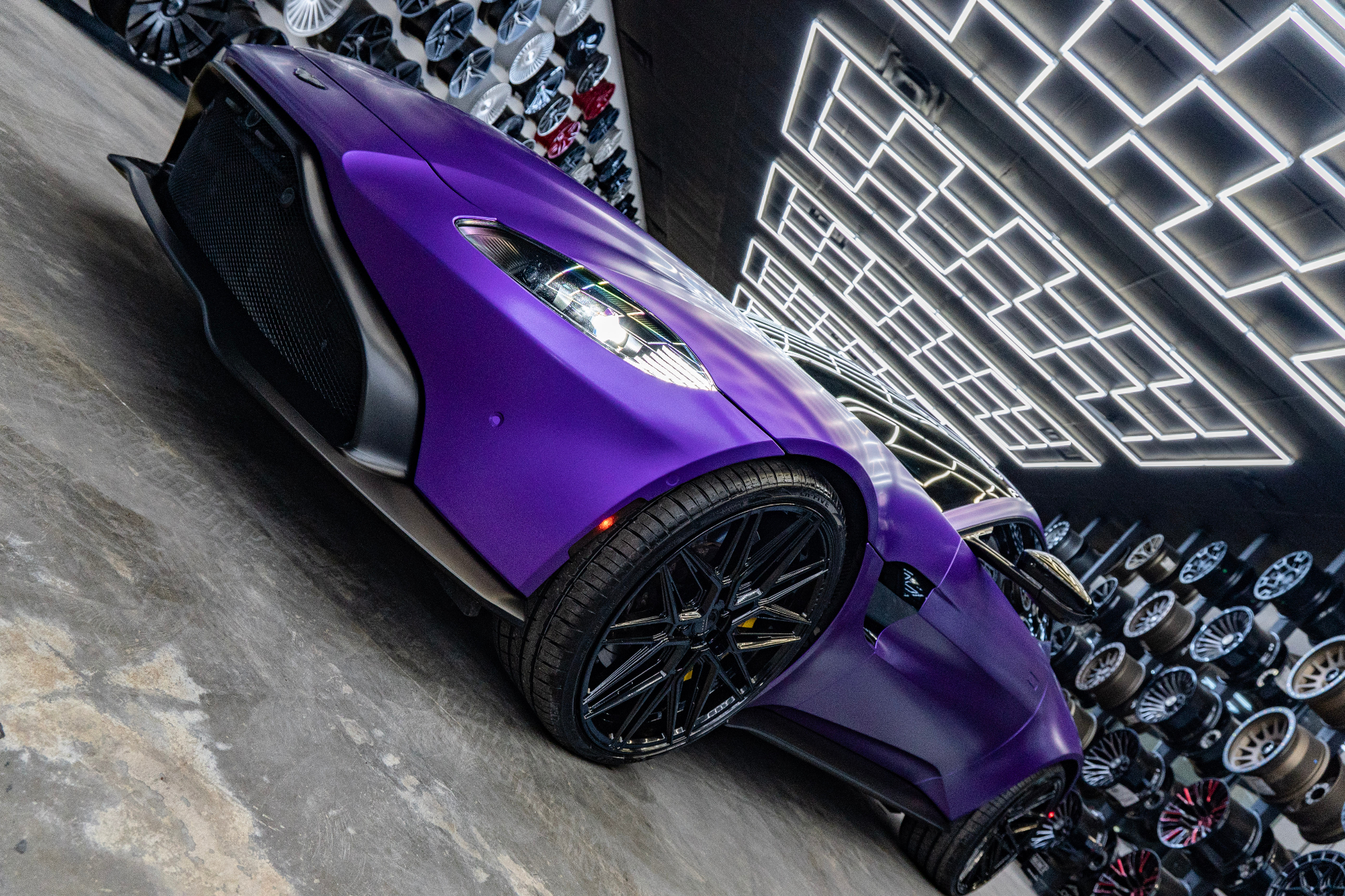 Low-angle front three-quarter detail of a satin purple Aston Martin Vantage on black custom wheels