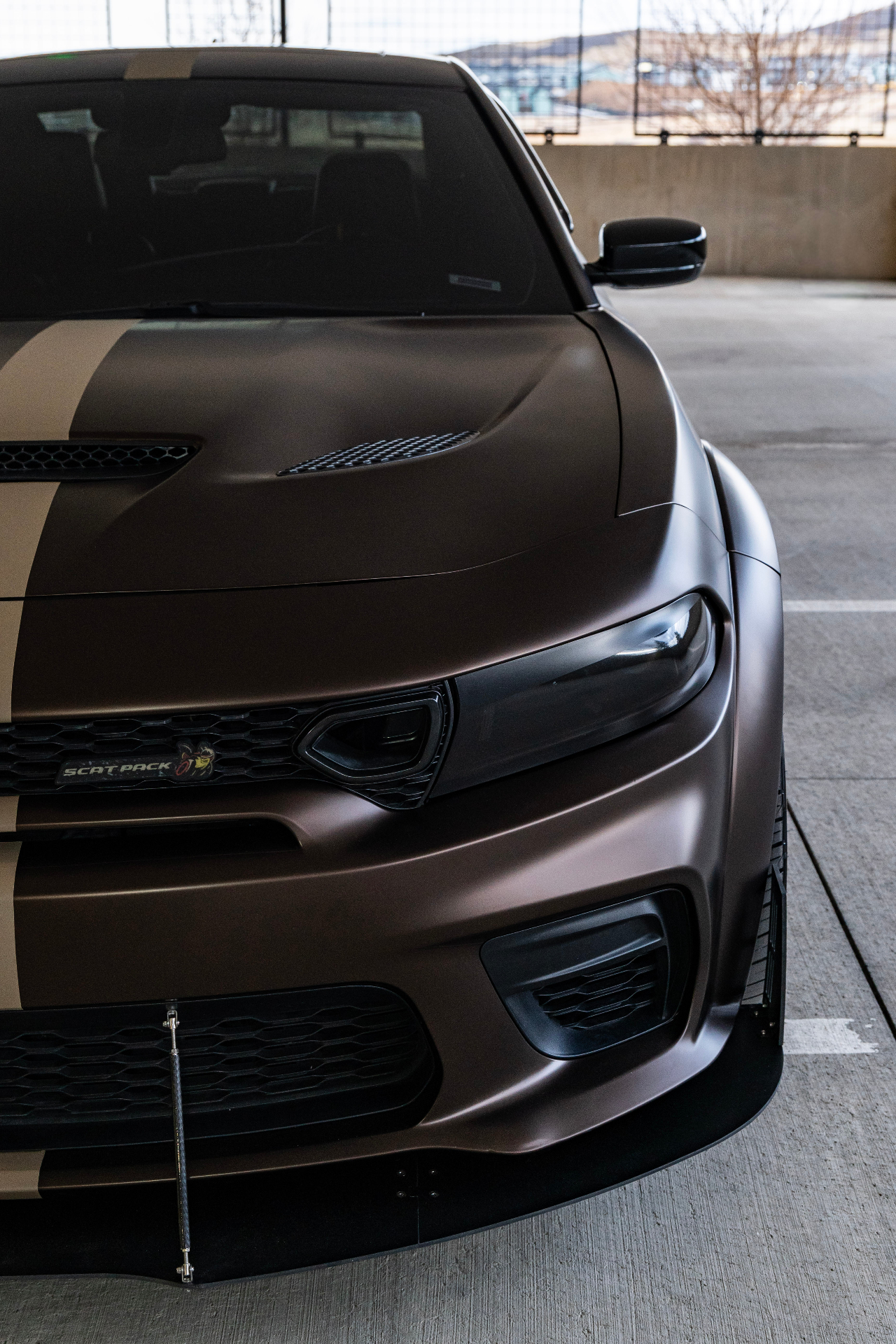 Front-end detail of matte brown Dodge Charger Scat Pack with tan stripes and splitter
