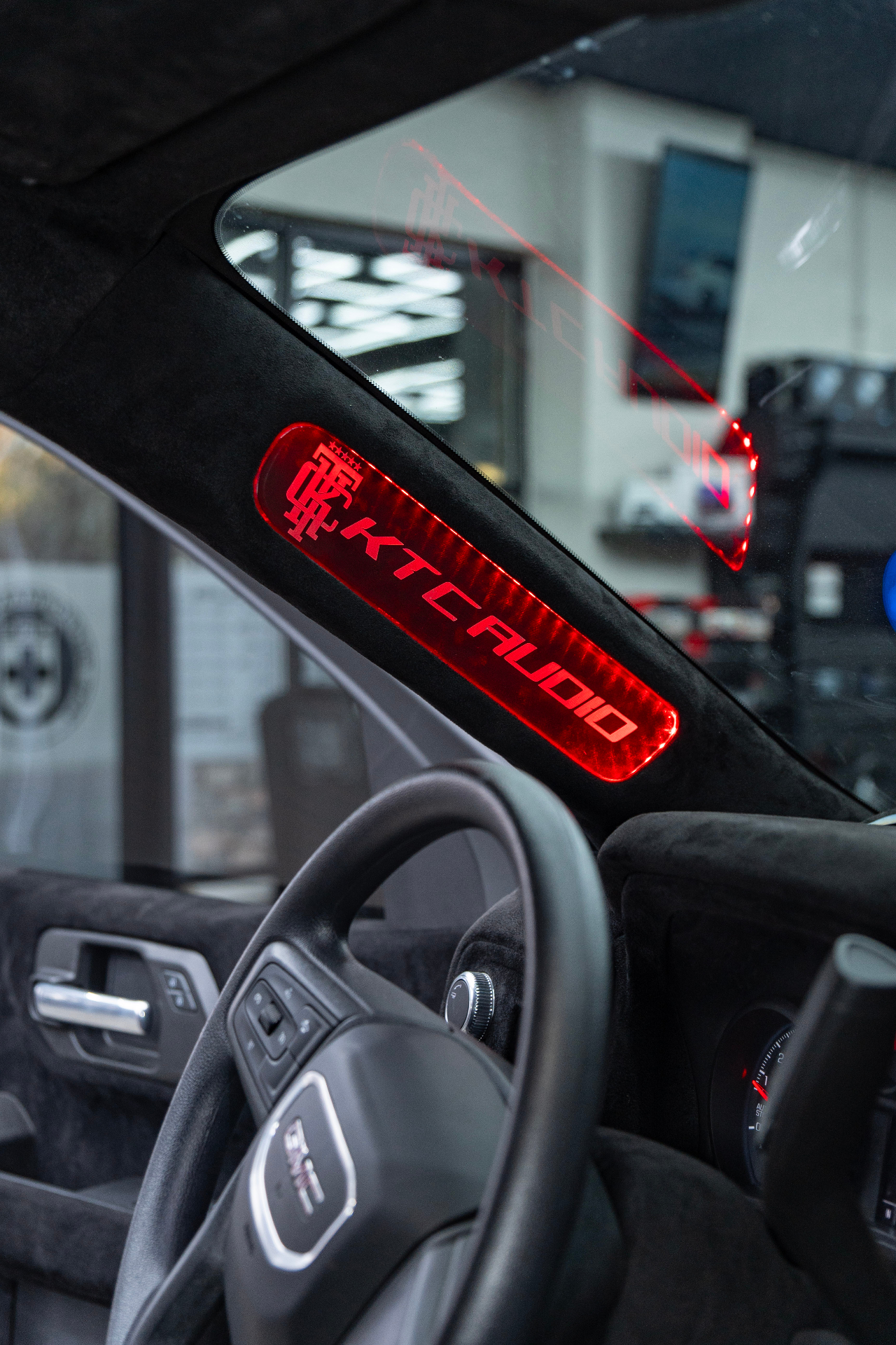 Illuminated KTC Audio badge on the A-pillar of a GMC Sierra interior