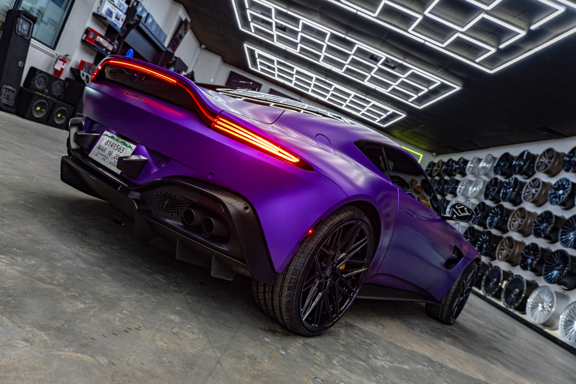 Rear three-quarter view of a satin purple Aston Martin Vantage with illuminated taillight inside the showroom
