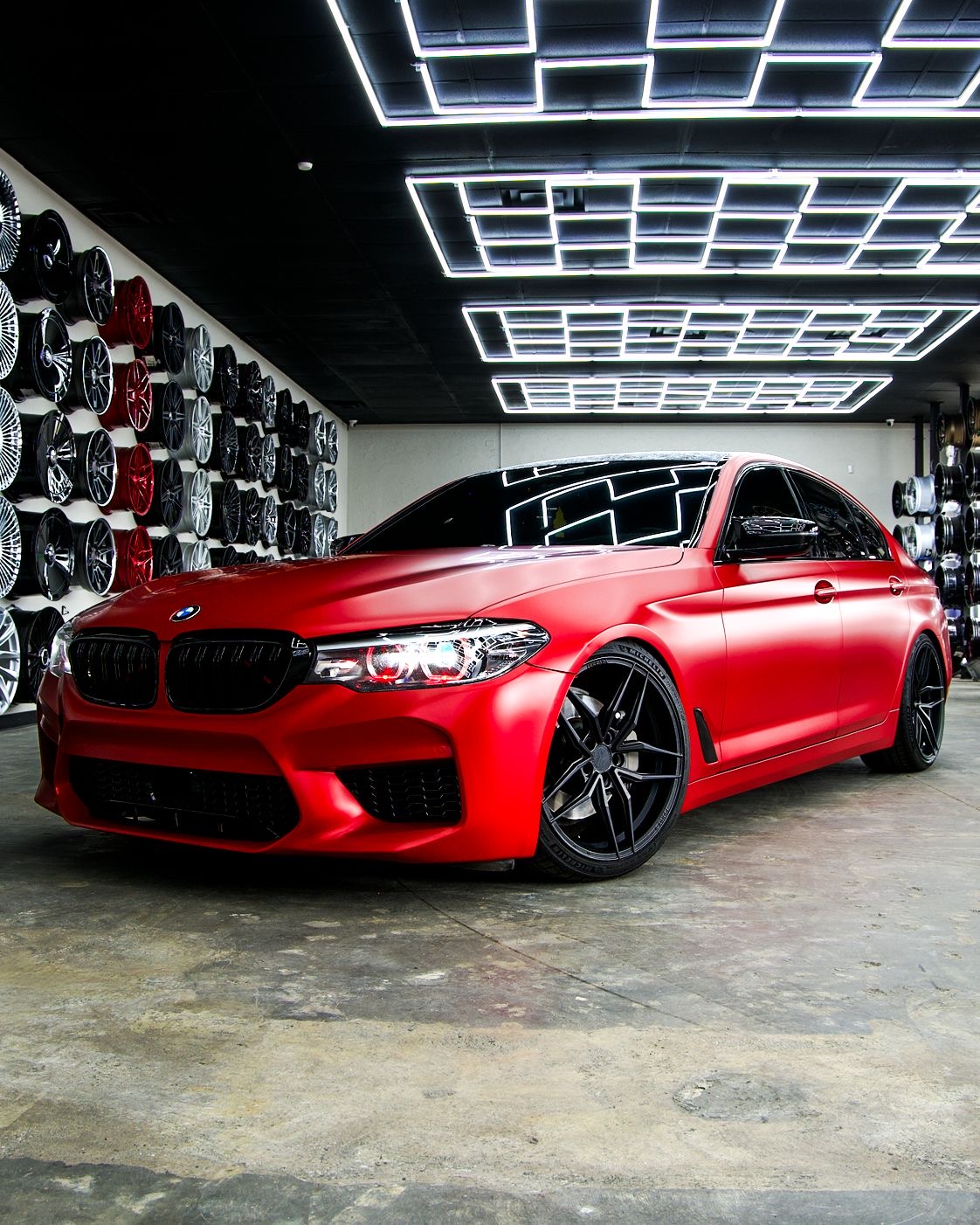 Matte red BMW M5 on custom black wheels in showroom