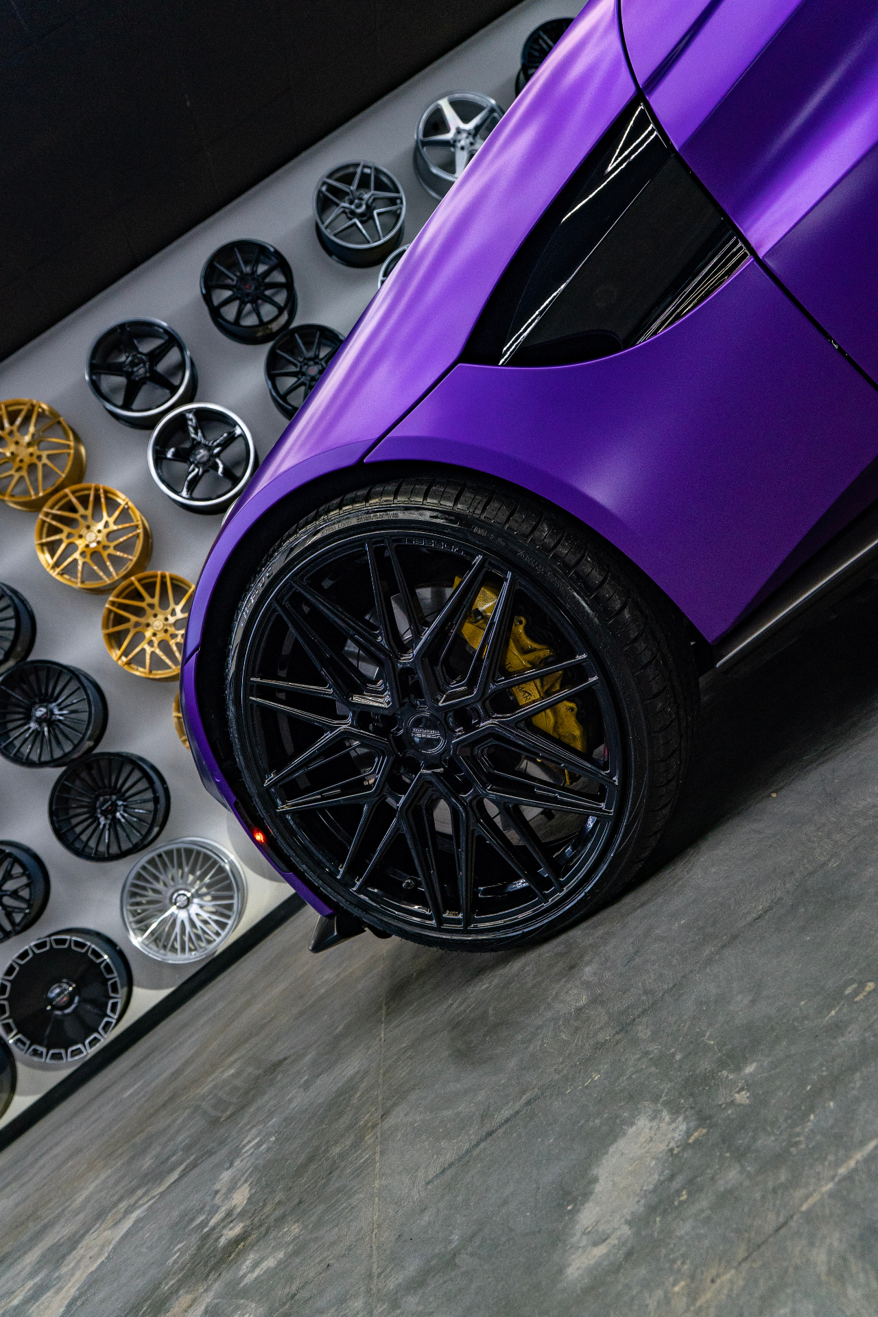 Close-up of the rear wheel and quarter panel on a satin purple Aston Martin Vantage in front of the wheel wall